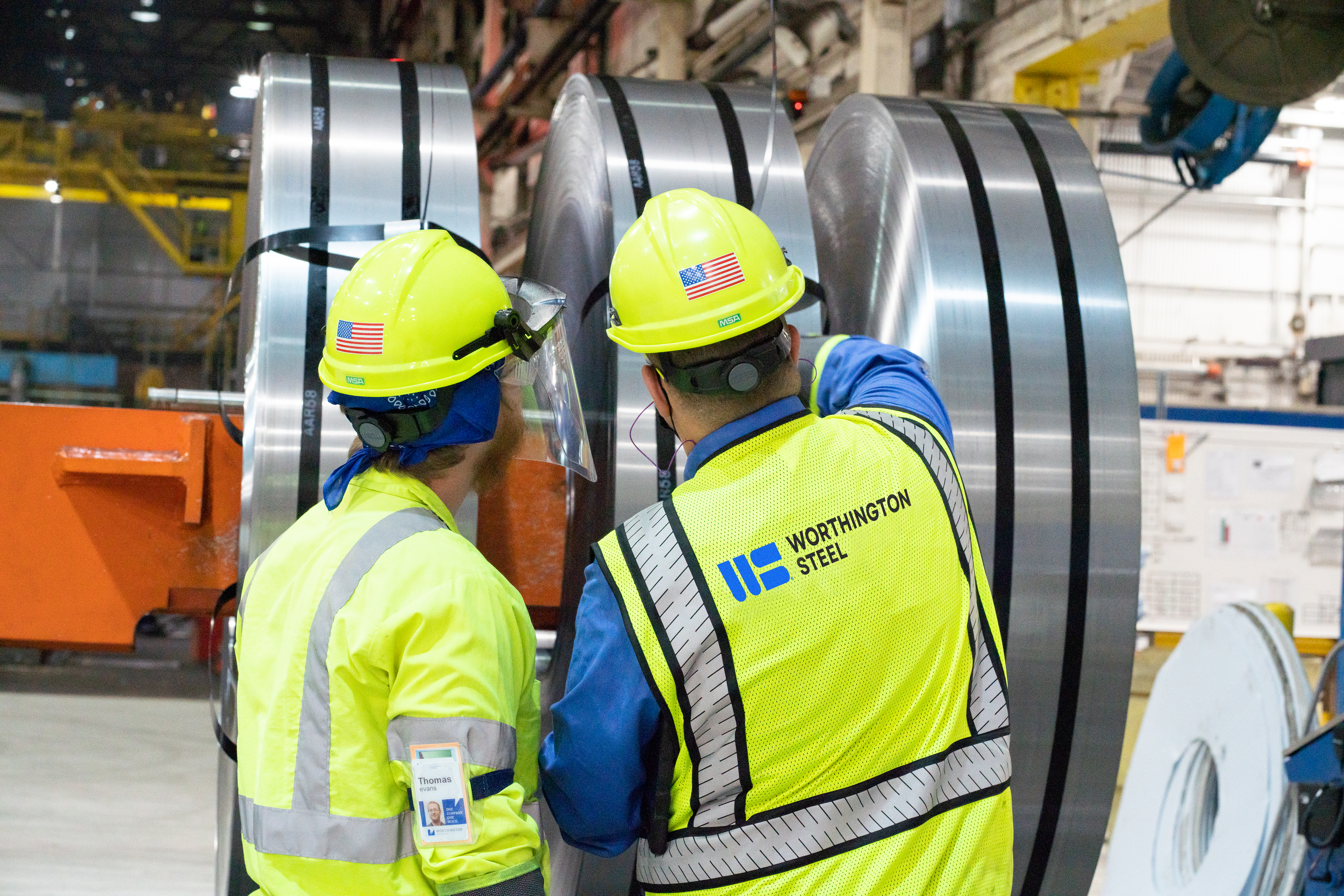 Worthington Steel employees inspecting large processed steel coils inside a steel processing facility.