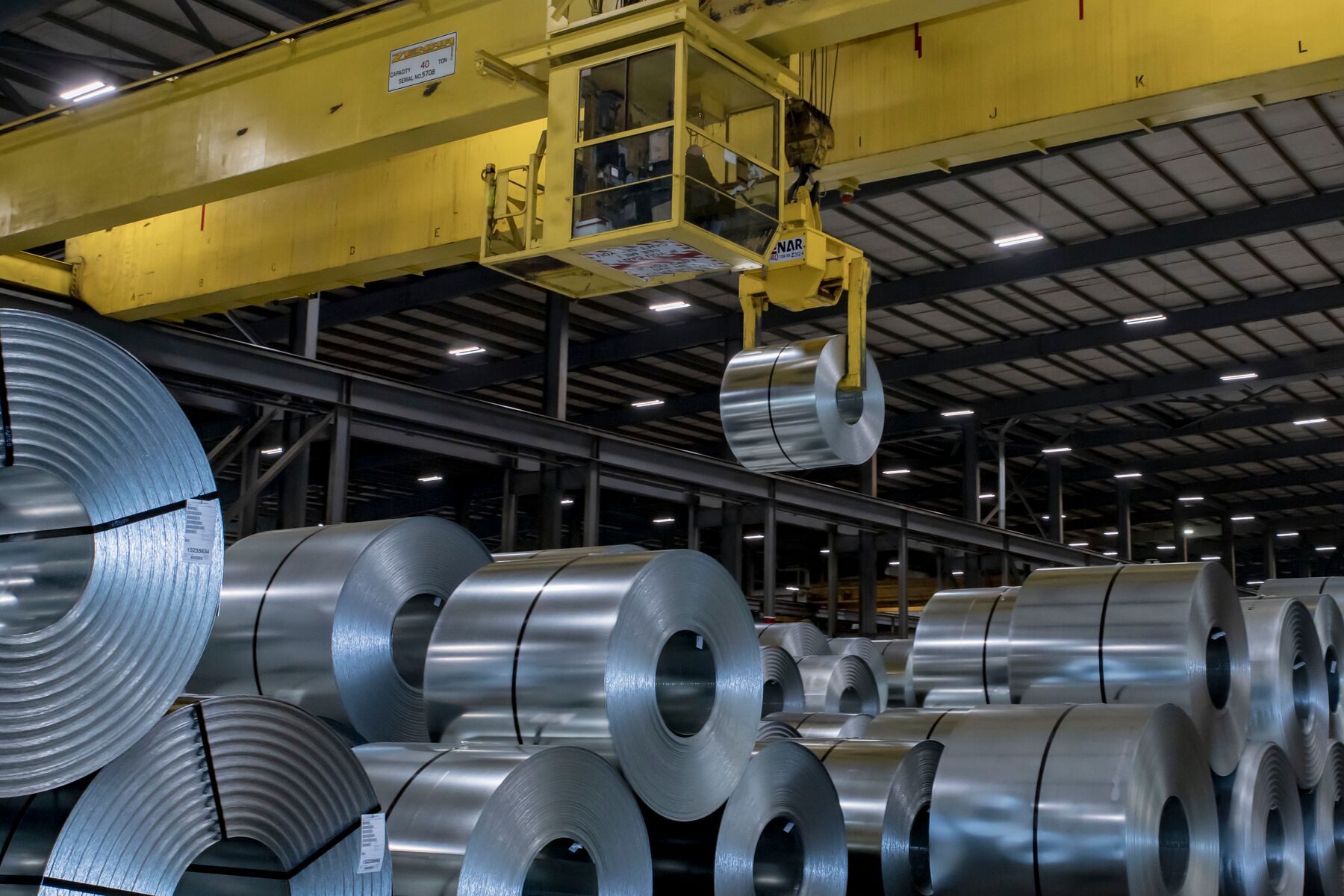 An overhead crane carrying a steel coil in a metals processing facility.