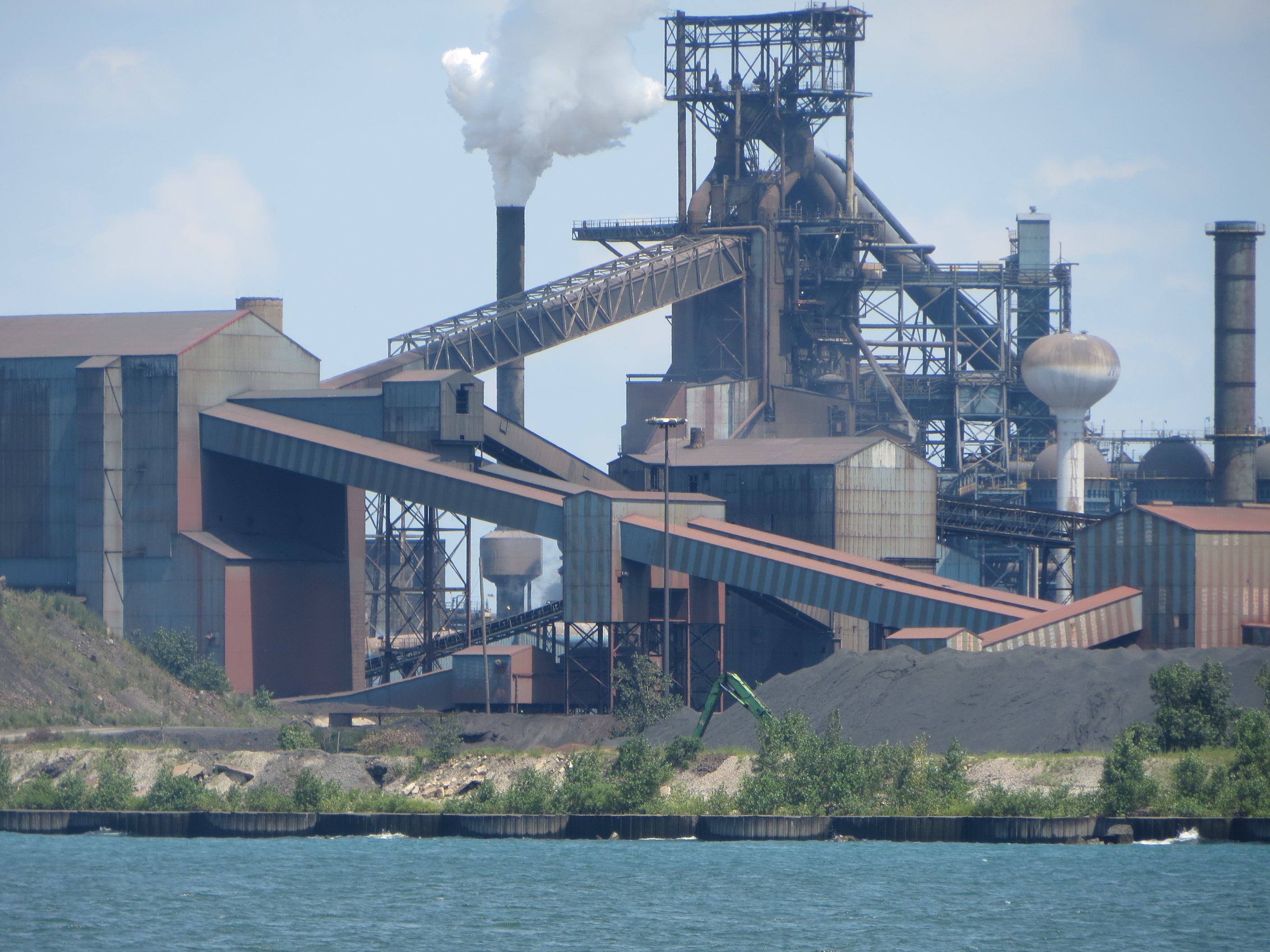 An operating integrated mill on the coast that has a plume of smoke coming out of the stack.
