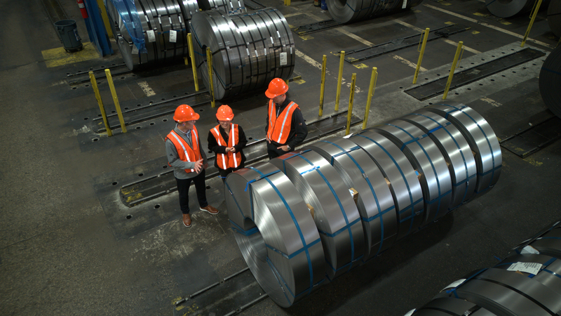 Seven bound slit galvanized coils being inspected by three Worthington Steel employees on the facility floor.