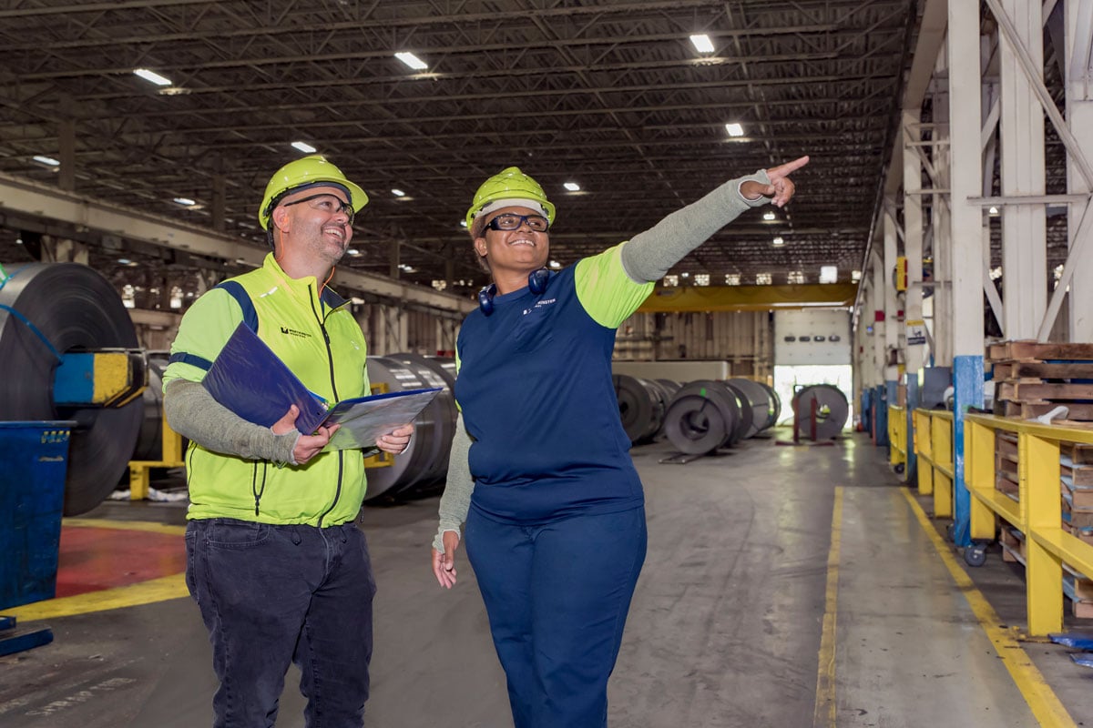 Employees reviewing work around the warehouse, pointing and holding binder