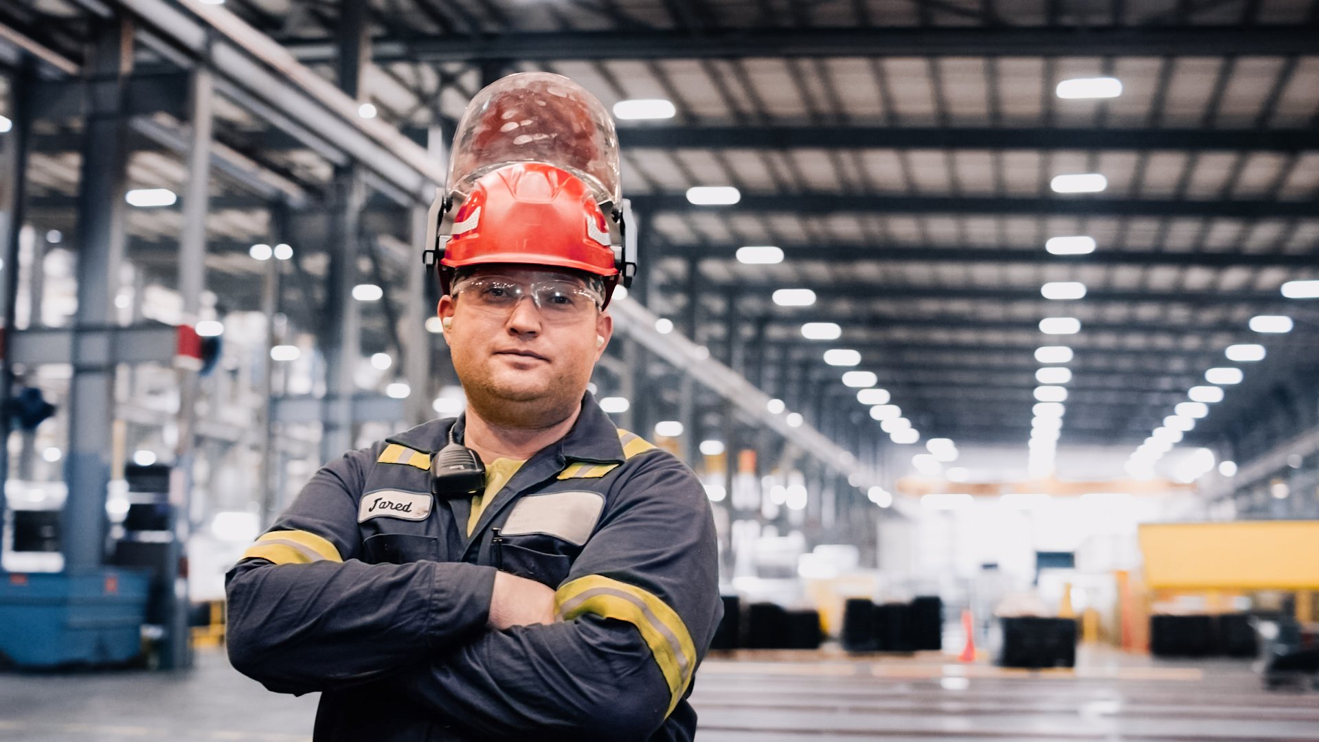 Employee with helmet and glasses on in warehouse staring into camera