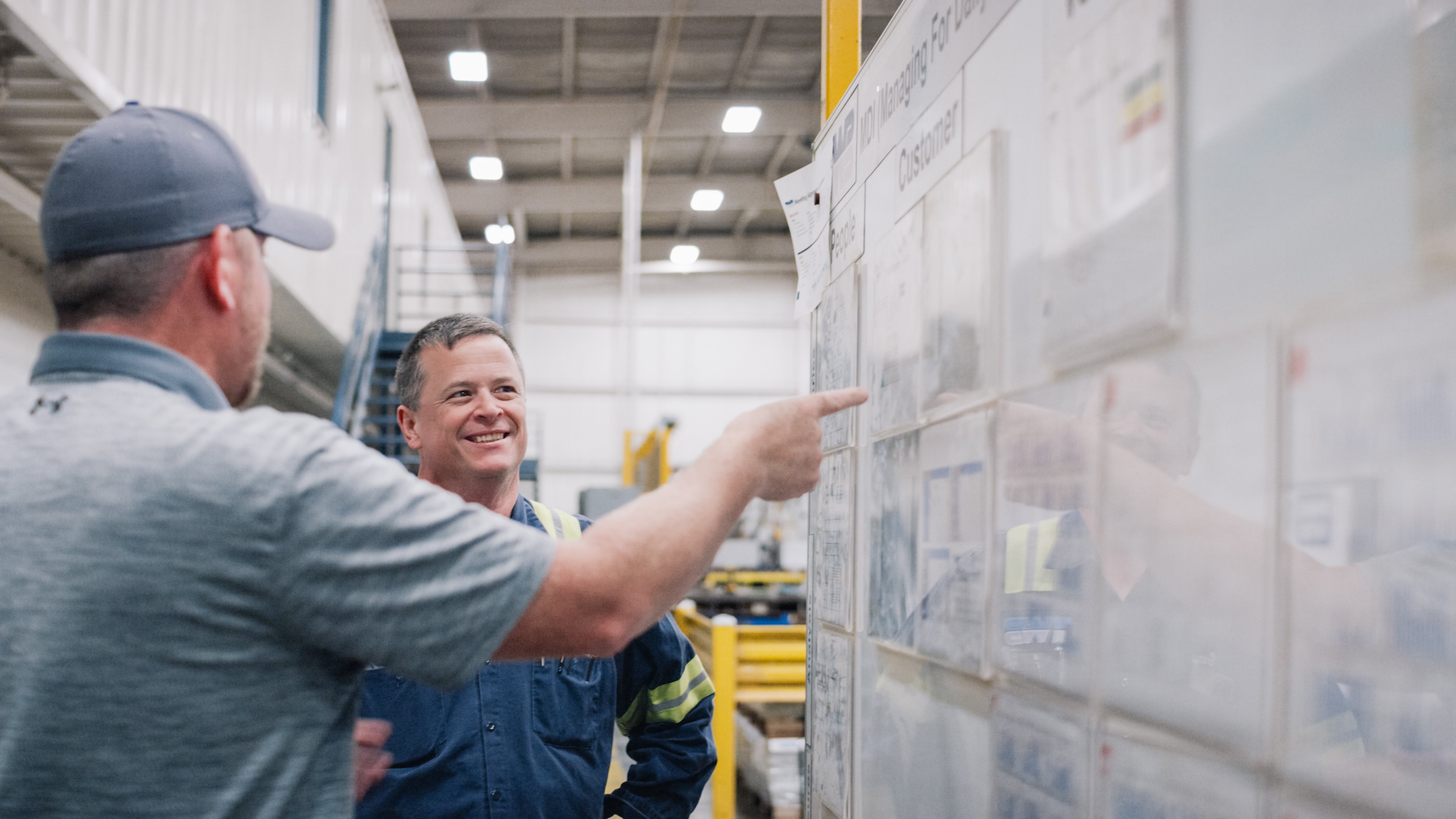 Worthington Steel coworkers smiling together as they look at a work board in steel processing facility.